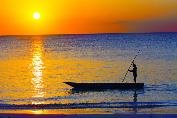 Beautiful sunset on Island of Zanzibar.   Local poling his way along the ocean.